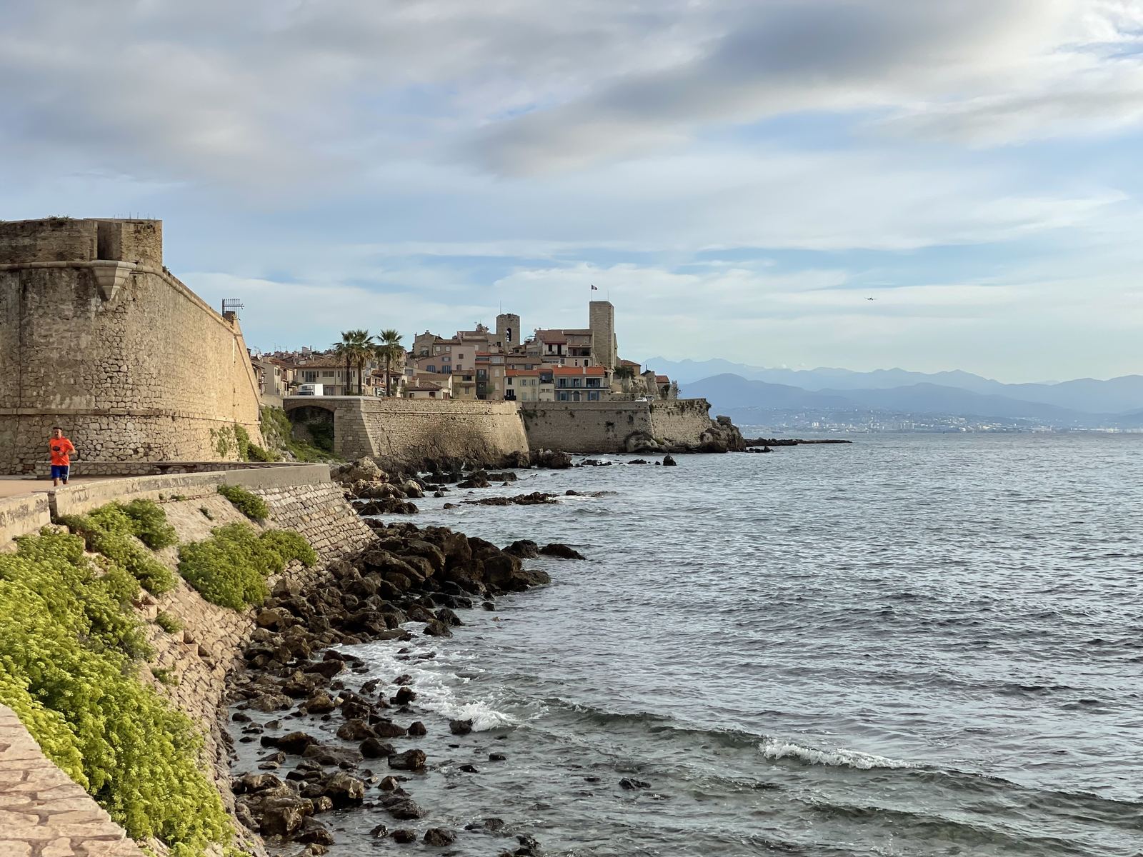 Antibes ramparts — the ancient seawall, a lone runner in red, the town stretching back along the coast